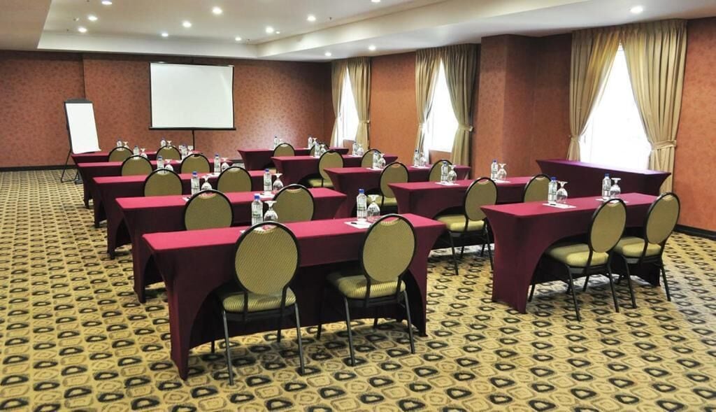 A conference room with multiple tables and chairs, a projector screen, and a carpeted floor.