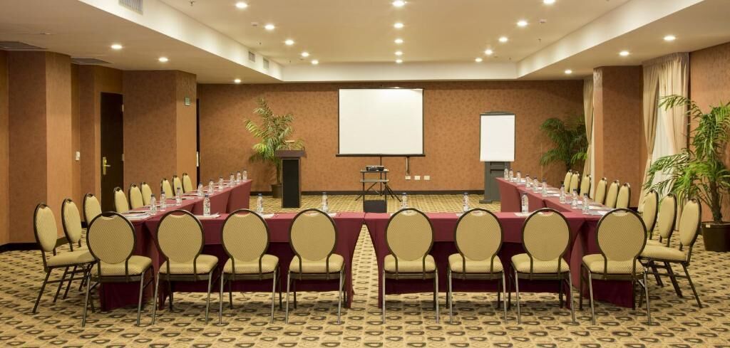 A conference room with a long table, chairs, a projector screen, and a carpeted floor.
