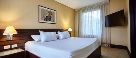 A hotel room with a large bed, two bedside tables with lamps, a flat-screen TV mounted on the wall, and a framed picture above the bed.