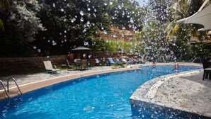 Una piscina con agua azul cristalina, rodeada de sillas de descanso y un pequeño pabellón.