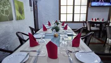 A dining area with tables set for service, featuring white plates, cutlery, and red napkins.