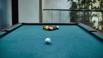 Una mesa de billar con una bola blanca y pelotas de colores, frente a un balcón con barandilla y vista a palmeras.