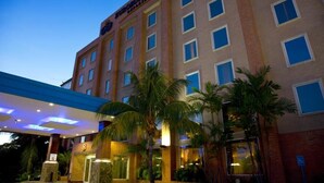Un hotel de varios pisos con un letrero llamativo, una entrada cubierta y palmeras al frente.