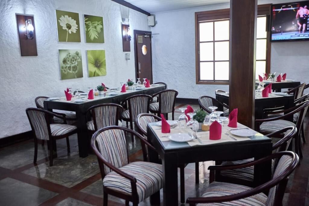 A dining area with multiple tables set for service, chairs with striped upholstery, and a large window providing natural light.