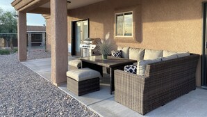Une terrasse extérieure avec un canapé en osier, une table et un barbecue.