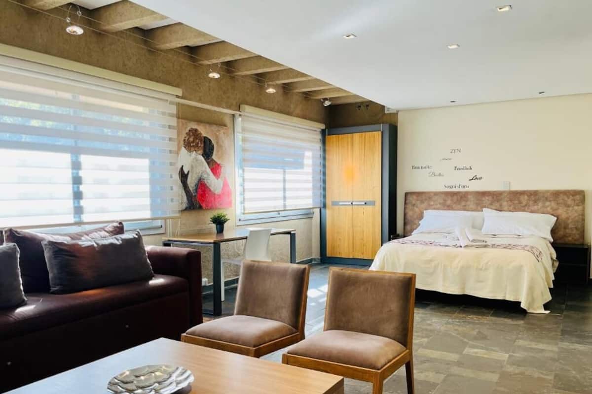 Una habitación de hotel moderna con una cama, una mesa de centro de madera, dos sillones y una mesa de comedor.