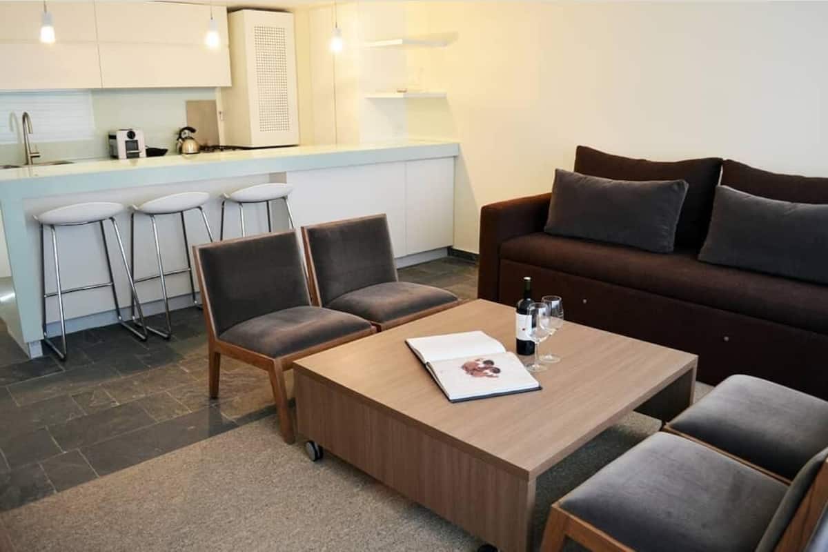 Una sala de estar moderna con un sofá, una mesa de centro y una zona de cocina con taburetes de bar.