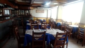 Een restaurant met meerdere tafels en stoelen, een bar met flessen en een raam dat natuurlijk licht binnenlaat.