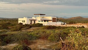 Uma casa moderna com telhado plano, um alpendre coberto e um veículo branco estacionado em frente.