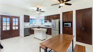 Uma cozinha moderna com armários de madeira, uma ilha central, eletrodomésticos de aço inoxidável e ventiladores de teto.