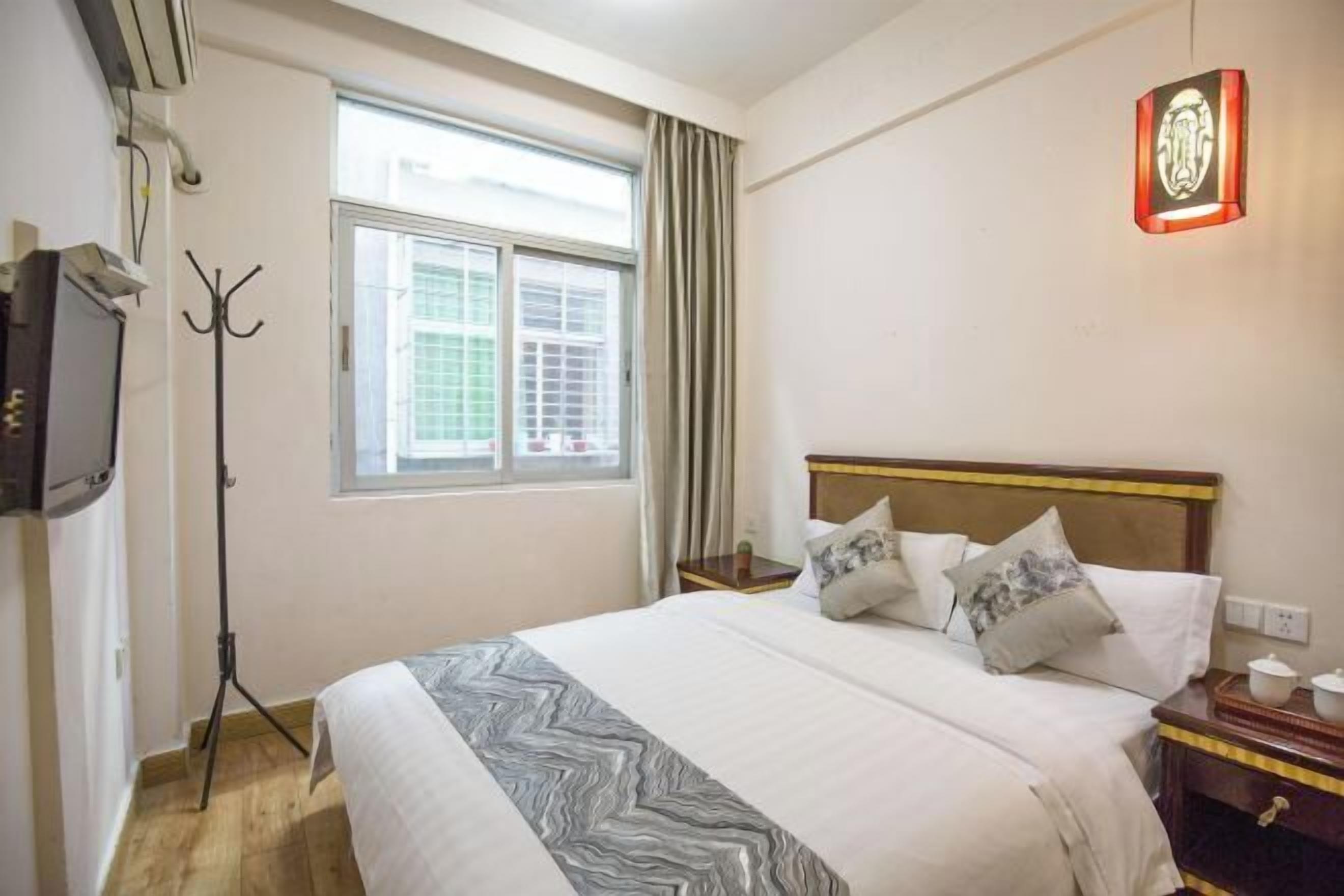 Hotelkamer met een bed, raam, kapstok, nachtkastje en een wandlamp.