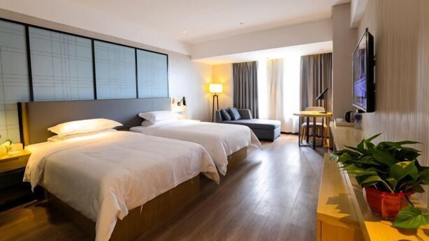 A hotel room with two beds, a sofa, a small table, a TV, and a potted plant. - Dongnan Express Hotel (Wuyishan)