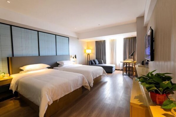 Habitació d'hotel amb dos llits, un sofà, una televisió, un escriptori i una planta.