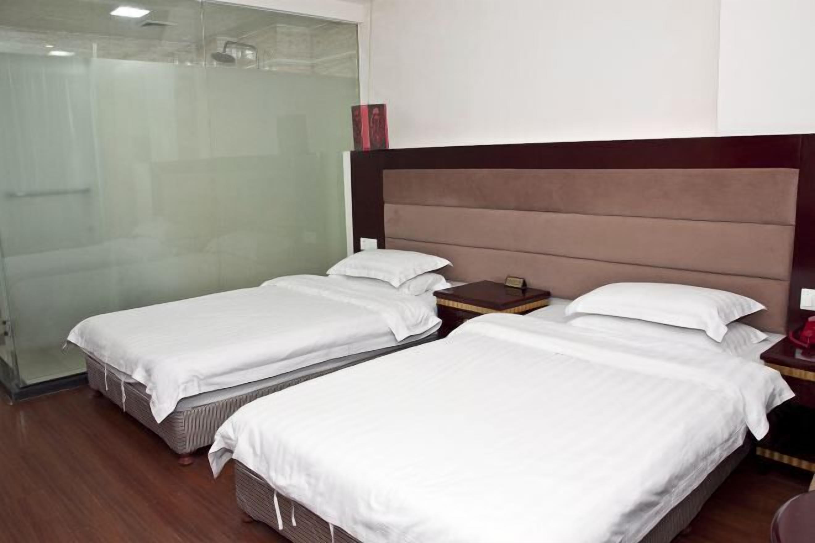 Une chambre d’hôtel avec deux lits simples, une tête de lit en bois, une table de chevet et une cabine de douche en verre.