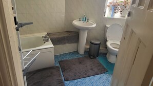 A bathroom with a bathtub, sink, toilet, and a window with a view of plants.