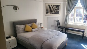 A neatly arranged bedroom with a bed, bedside table, lamp, chair, and a framed picture on the wall.