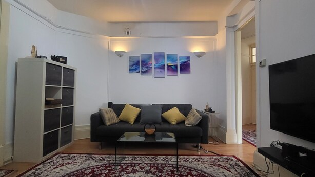 A living room with a black sofa, a coffee table, a TV, a bookshelf, and wall art.