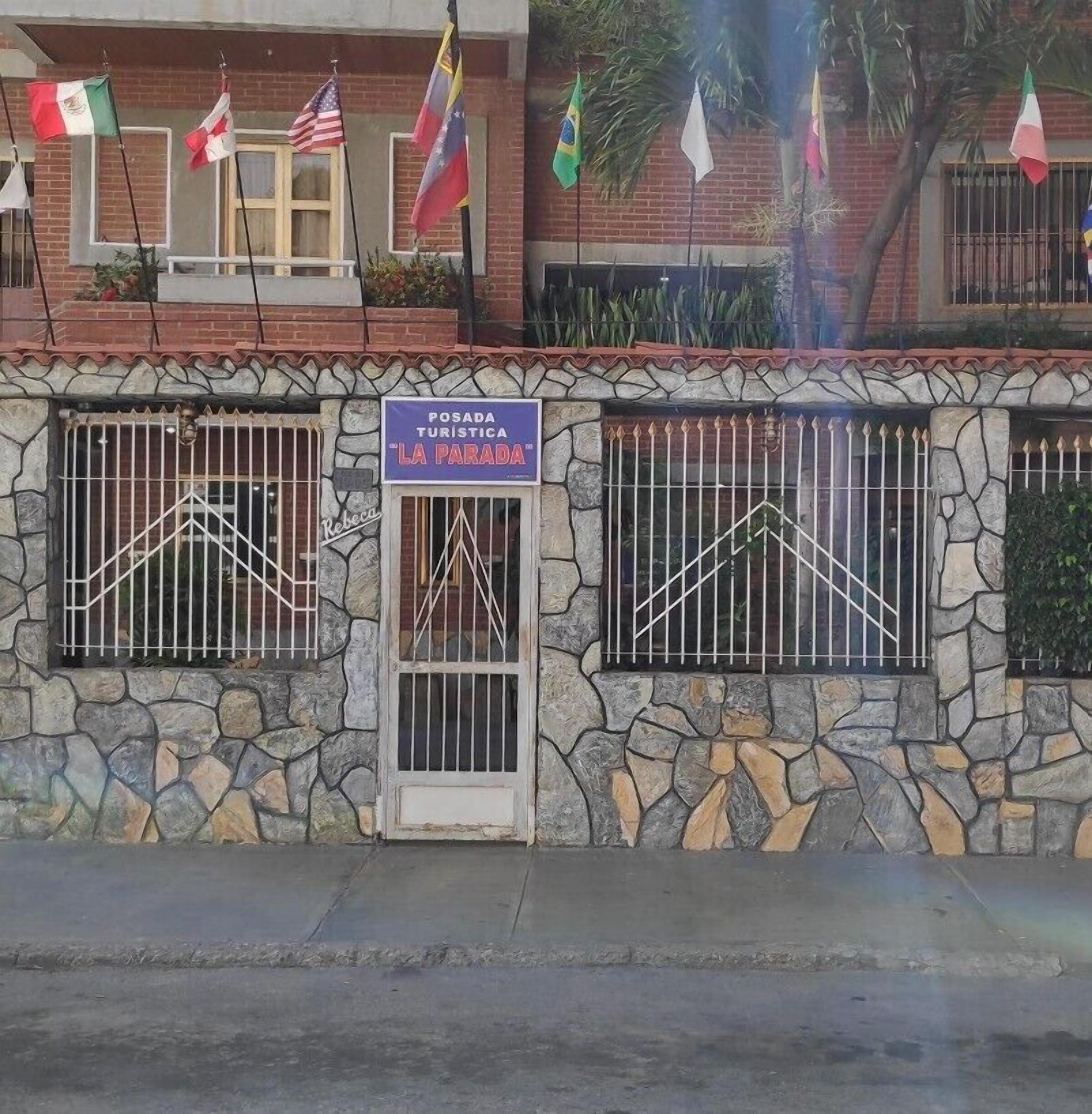 A building with a stone facade, a sign for 'Posada Turistica La Parada', and multiple flags including the Mexican and American flags.