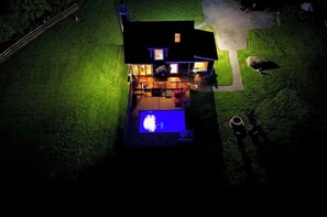 A house with a swimming pool, a covered patio, and a fenced yard at night.