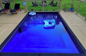 A swimming pool with a blue inflatable float, lounge chairs, and a fire pit on a wooden deck.