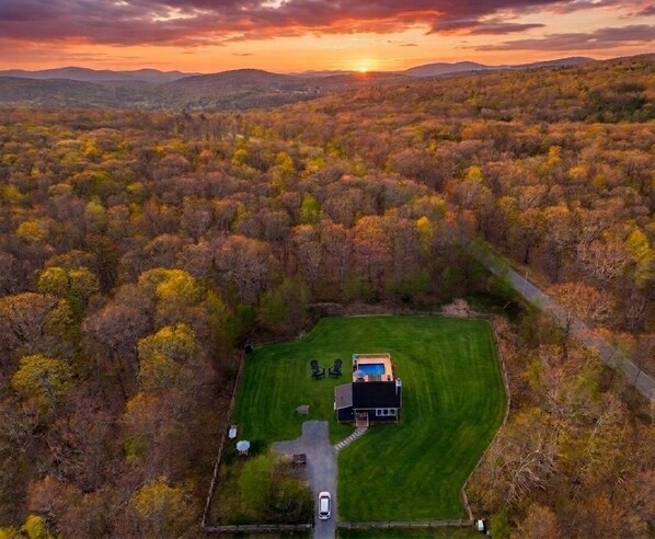 An aerial view of a property with a house surrounded by a well-maintained lawn and dense forest.