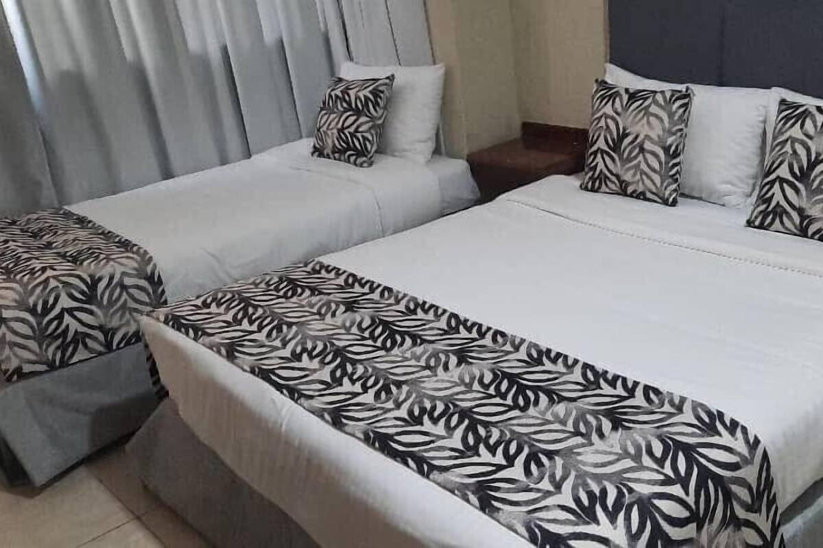 A double bed with a patterned bedspread, two bedside tables, and a nightstand with a lamp.