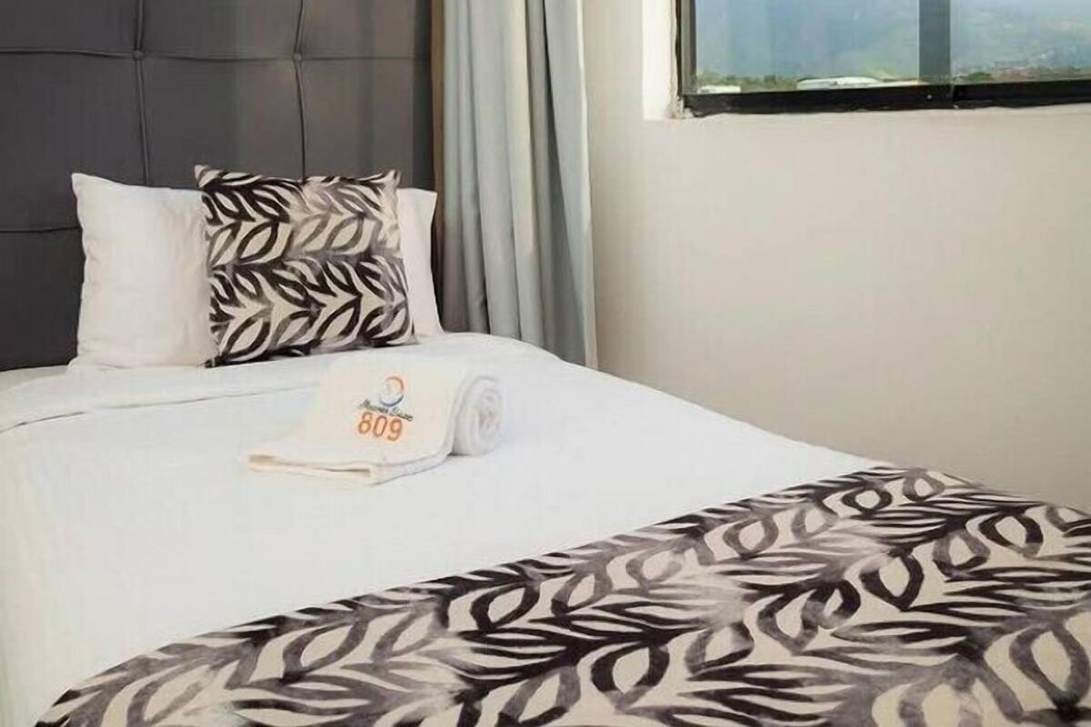 A hotel room with a bed, a window with a view, and an air conditioning unit.