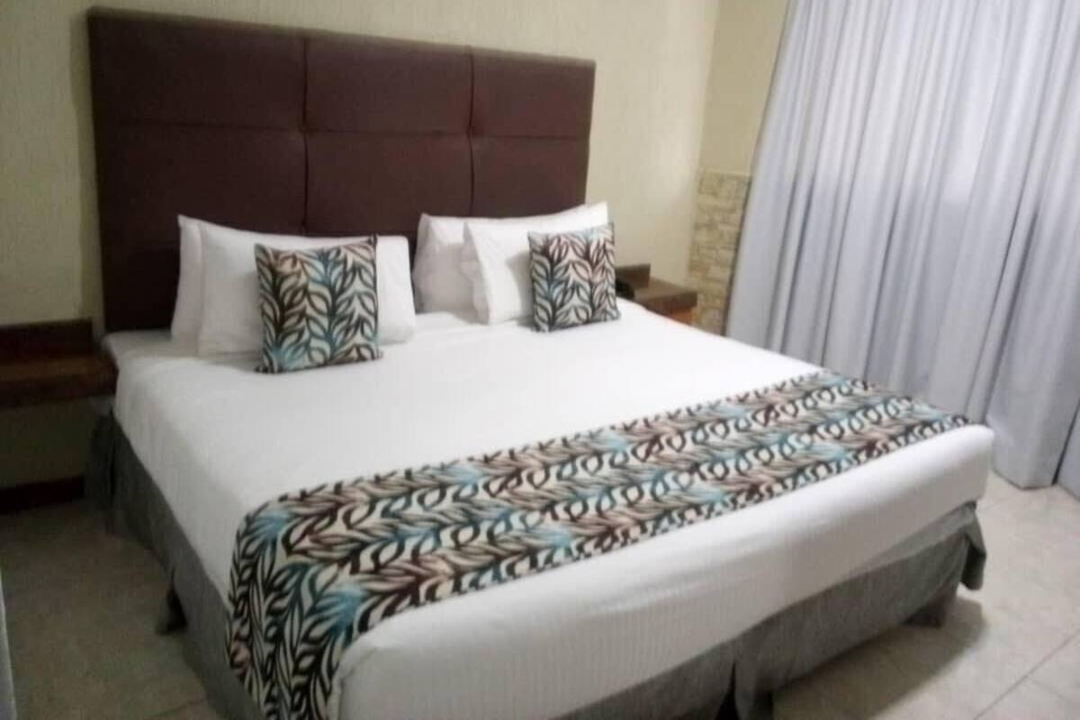 A hotel room with a large bed, a headboard, and a window with curtains.