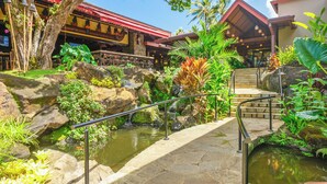 Ein tropisches Resort mit einer Steinkonstruktion über einem Teich, umgeben von üppiger Vegetation und einem Restaurant mit rotem Dach.