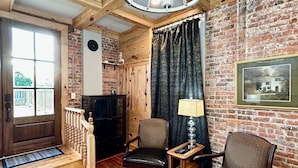 A cozy room with wooden floors, a brick wall, a chandelier, two leather chairs, a small table with a lamp, and a framed picture on the wall. - Room 1 (sleeps 1) at Chipley's Squareview Inn (Carthage)