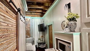 A narrow hallway with wooden beams on the ceiling, a white door on the right, and a white cabinet with a microwave on the left. - Room 1 (sleeps 1) at Chipley's Squareview Inn (Carthage)