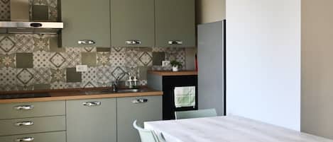 Uma cozinha com armários verdes, bancada de mármore e mesa de jantar com cadeiras.