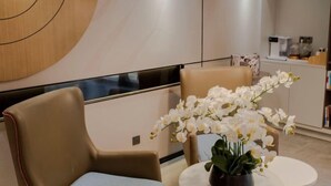 Un espace d’attente moderne avec une table ronde, deux chaises et un panneau décoratif fixé au mur.