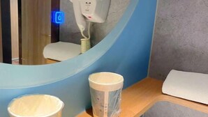 Une salle de bain avec un miroir rond, un sèche-cheveux et deux tasses posées sur une étagère en bois.