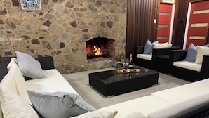 Un mur en pierre avec une cheminée, une table basse noire sur laquelle se trouve un plateau de nourriture et de boissons, et deux canapés avec des coussins.
