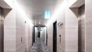 Ein moderner Hotelkorridor mit Teppichboden, hellen Wänden und Türen an beiden Seiten.