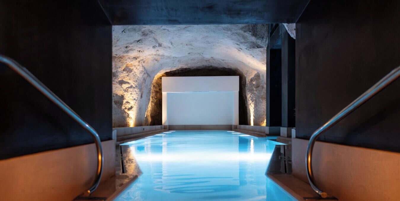 Piscina interna com parede de pedra e uma grande tela branca ao fundo.