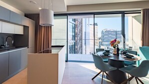 Une cuisine moderne dotée d’un îlot central, un coin repas avec une table ronde et des chaises, et une grande porte-fenêtre coulissante donnant sur un balcon avec vue sur la ville.