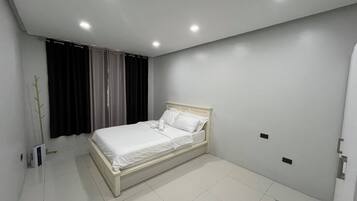 Une chambre à coucher avec un lit, des rideaux, un radiateur et un luminaire fixé au mur.