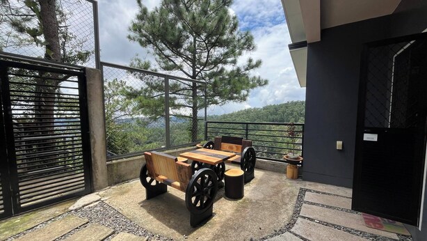 An outdoor patio with a wooden table and chairs, surrounded by a stone pathway and a metal fence. - A quiet and amazing place with mountain view and cool breeze of Baguio City. (Baguio City)