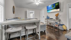 A modern kitchen with a bar area, a ceiling fan, and a large TV displaying a beach scene. - Classy 4BR Family Home Near FSU (Tallahassee)