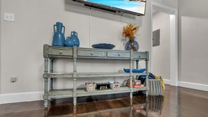 A wooden console table with multiple shelves, a vase with dried flowers, and a basket with items on a wooden floor. - Classy 4BR Family Home Near FSU (Tallahassee)
