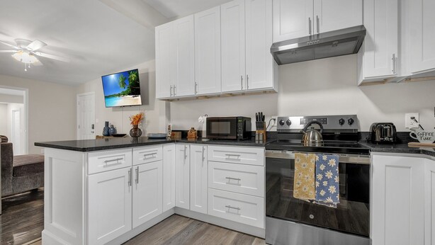 A modern kitchen with white cabinetry, a stainless steel oven, a microwave, and a gas stove. - Classy 4BR Family Home Near FSU (Tallahassee)