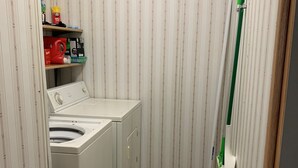 Kompakti pyykinhuoltotila, jossa on pesukone, pyykkiteline ja hylly, jossa säilytetään siivoustarvikkeita.