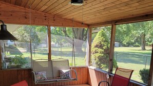 A covered patio area with wooden walls, a cushioned bench with pillows, and several chairs. - Cute, pet-friendly home in quiet neighborhood. Close to state parks & downtown. (Rockville)