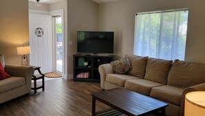 A living room with a sofa, a coffee table, a TV, and a lamp. There is a door leading to another room. - Cute, pet-friendly home in quiet neighborhood. Close to state parks & downtown. (Rockville)