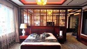 Una habitación de hotel con una cama, una mesita de noche, una lámpara, un biombo decorativo y vistas al pasillo.