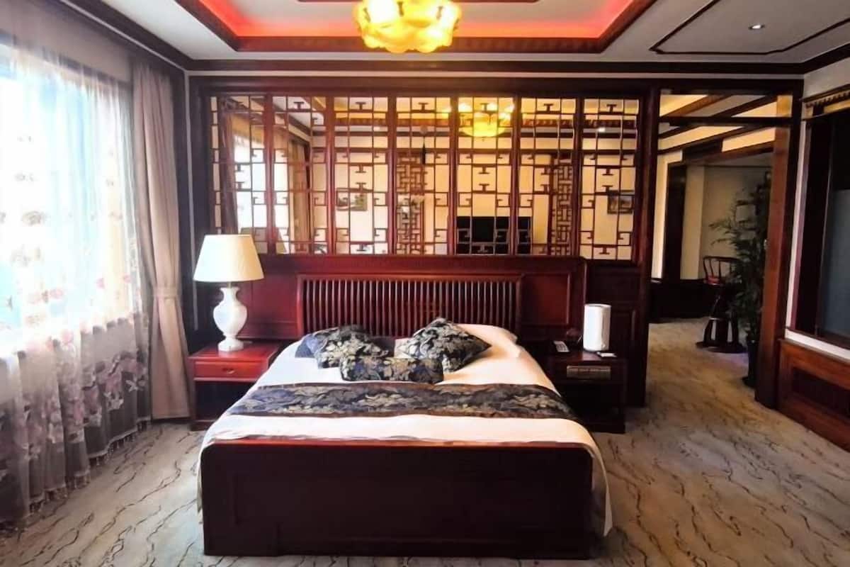 Een hotelkamer met een bed, nachtkastje, lamp, decoratieve roomdivider en uitzicht op de hal.