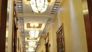 Un largo y estrecho pasillo con suelo de mármol brillante, luces de techo con diseños y obras de arte enmarcadas en las paredes.
