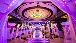 Un pasillo de hotel con una escalera central, cortinas con drapeados y candelabros.